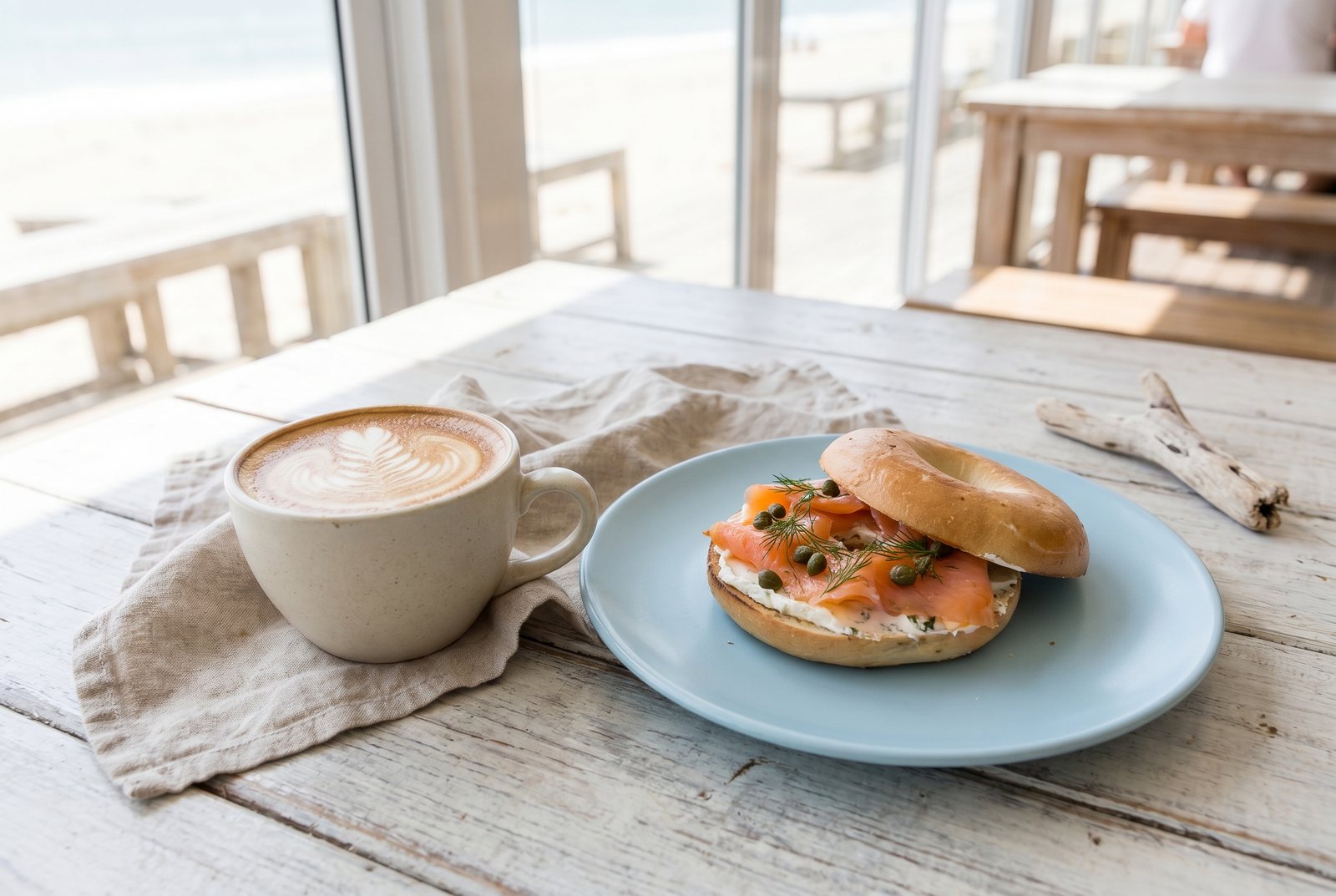 A latte and a bagel on a bright cafe table