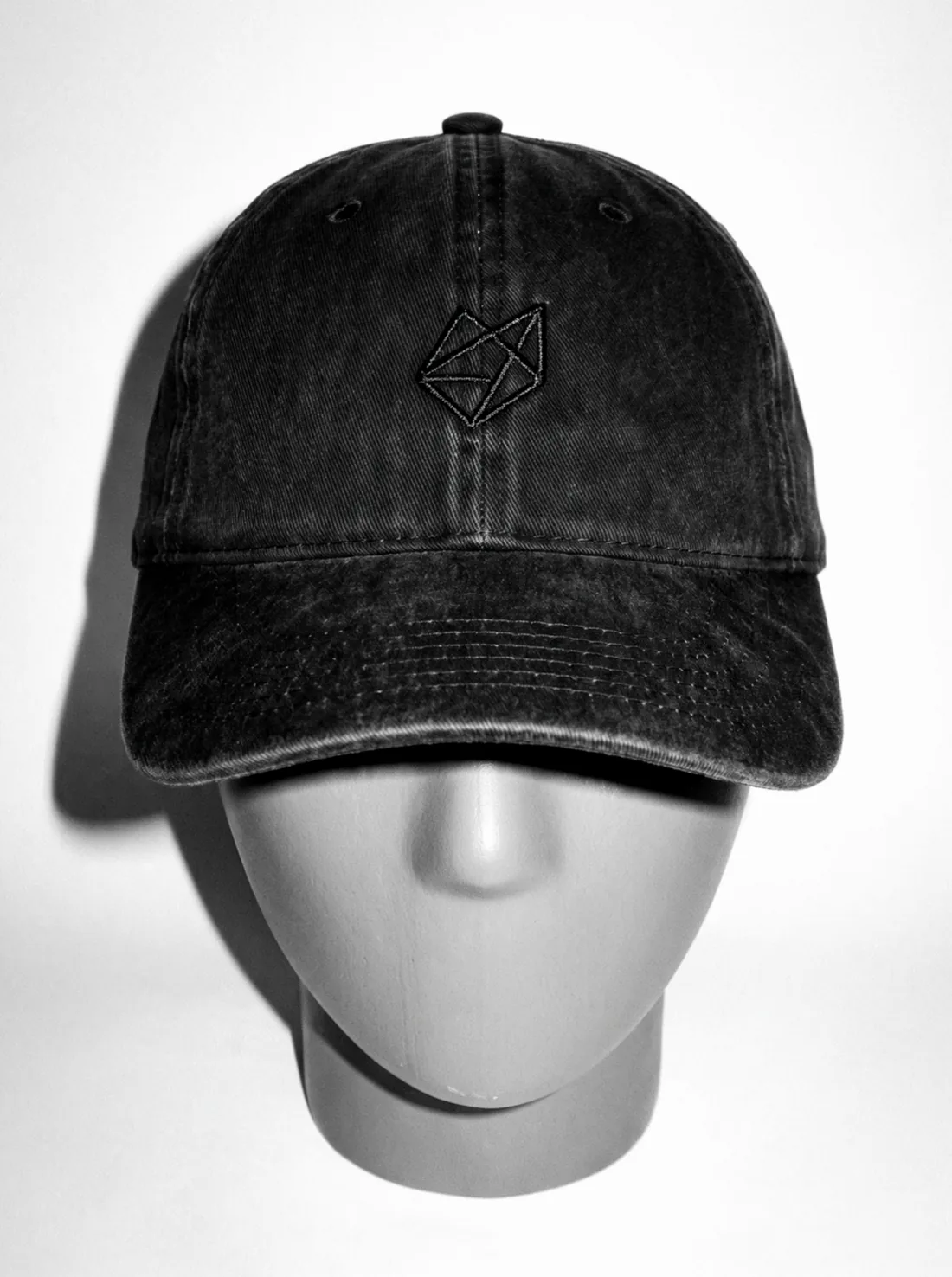 The Palletcap on a head form, front on, its tonal embroidered mark catching the flash, frame one of its turn