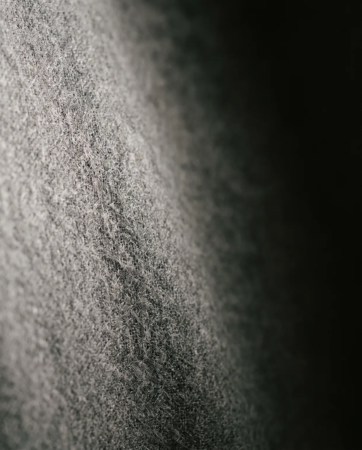 Macro of mid-grey flannel, the brushed nap catching a low side light before the cloth falls to black