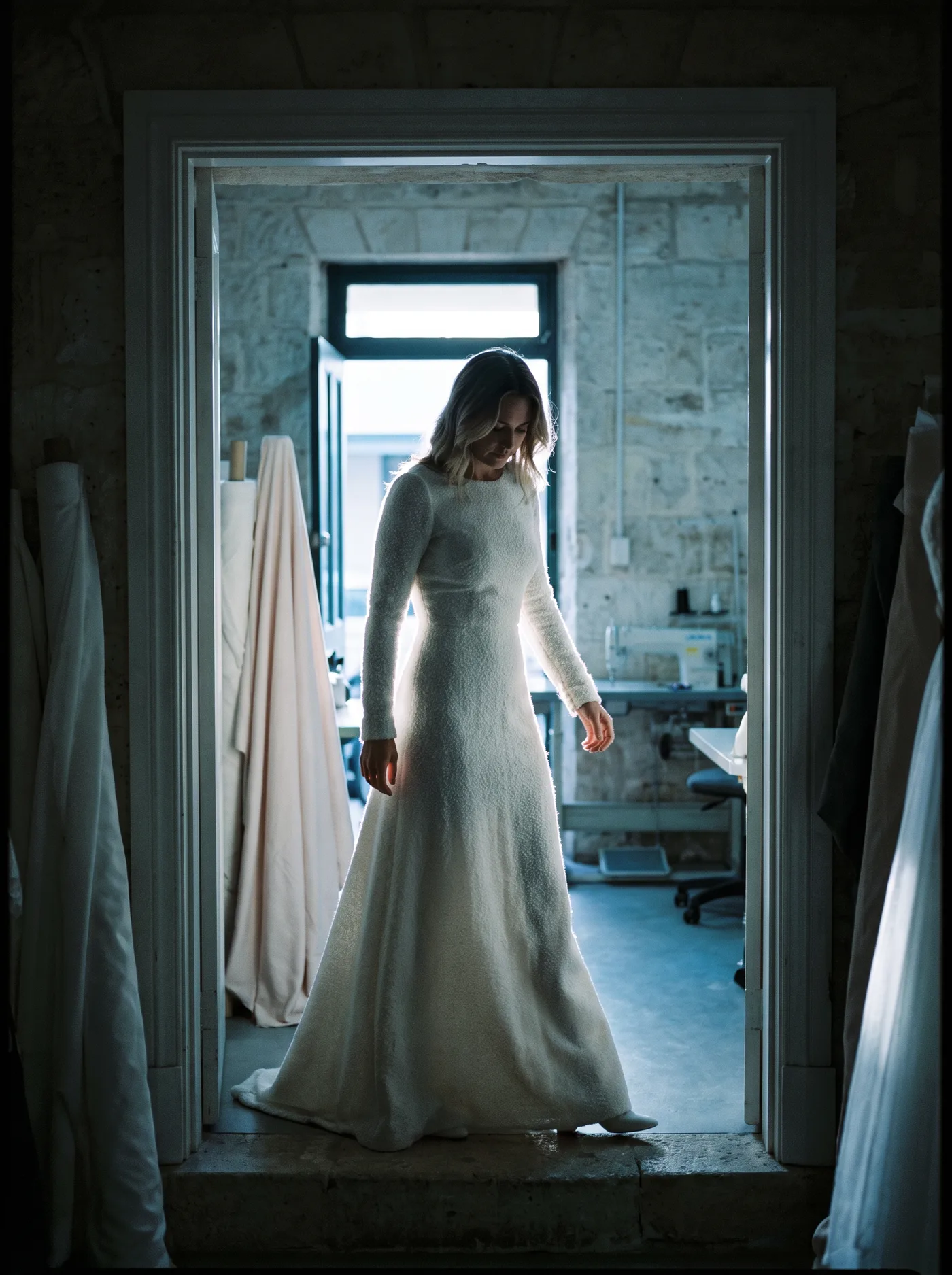 Look 06, a long-sleeved wool gown backlit in a doorway.